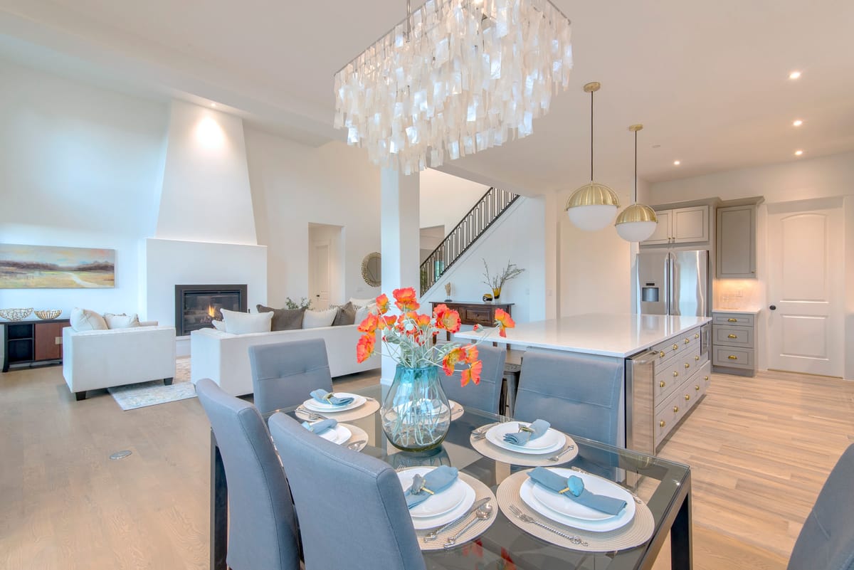 A dining table set for four beside the kitchen, under a crystal chandelier