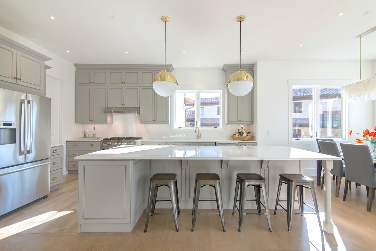 A white kitchen with a marble island, bar stools and pendant lights