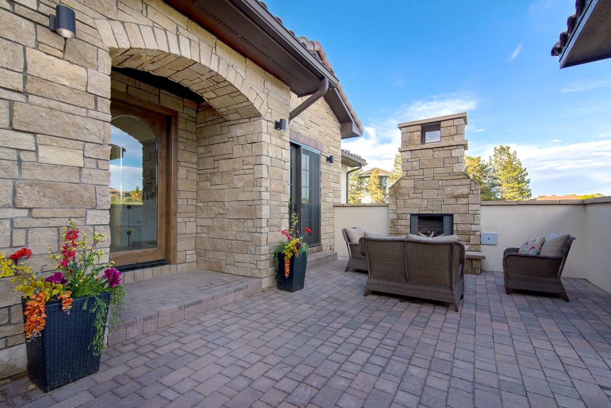 A covered stone patio with an outdoor fireplace and lounge seating