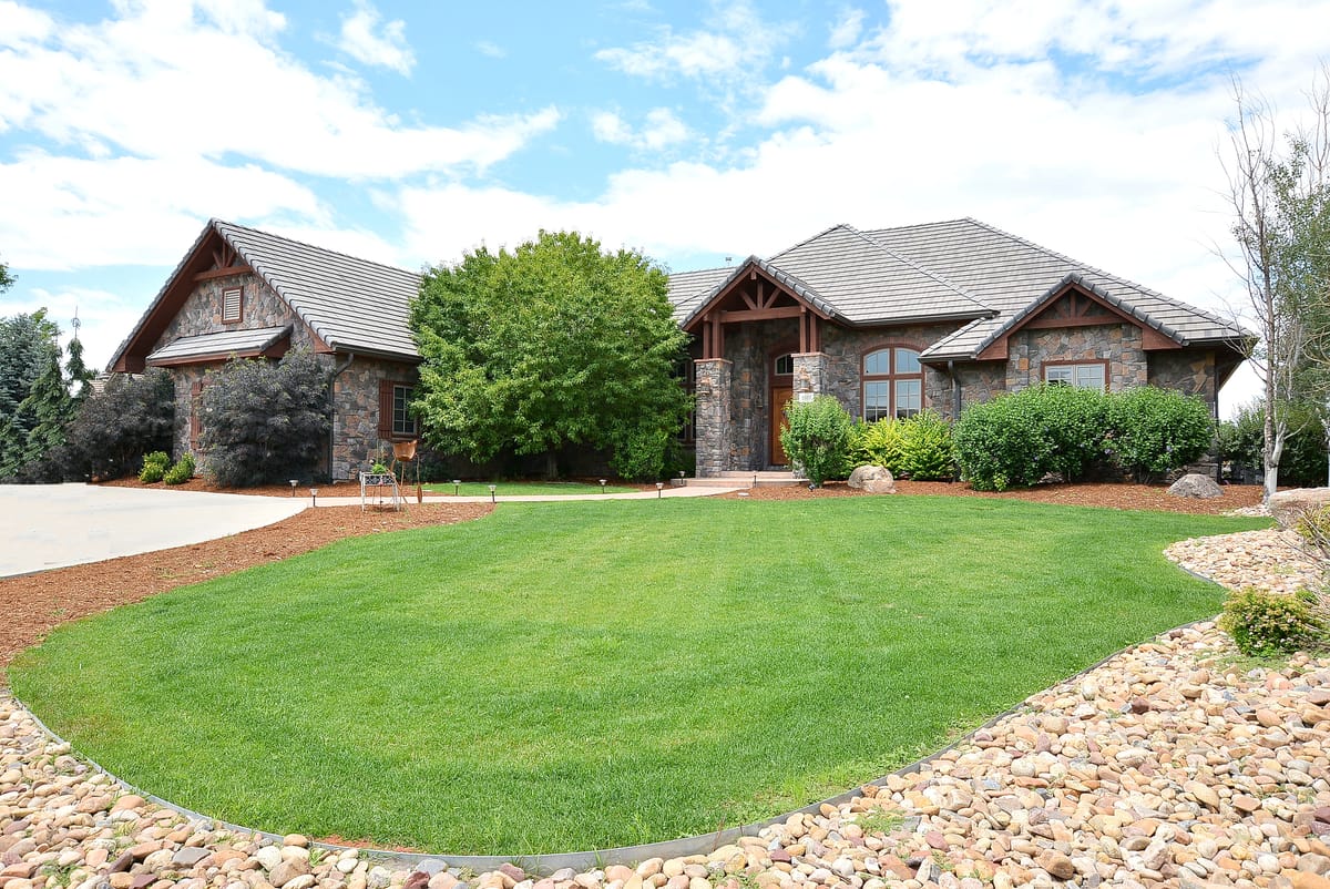A stone and shingle ranch home behind a broad lawn