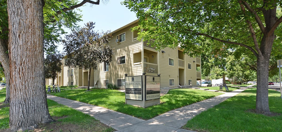 A three-storey apartment building among mature trees, seen from a walkway