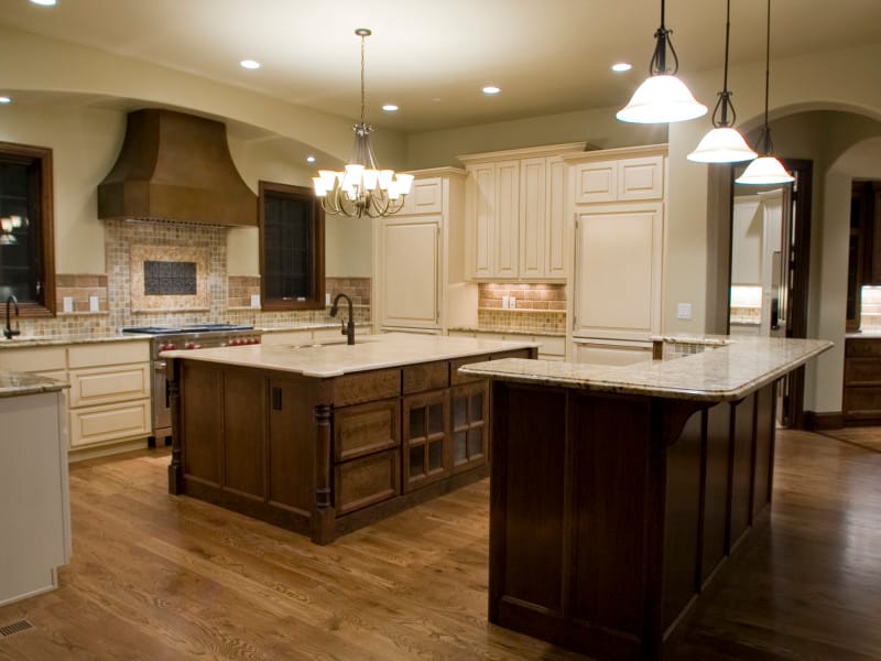 A kitchen with a dark wood island, range hood and chandelier