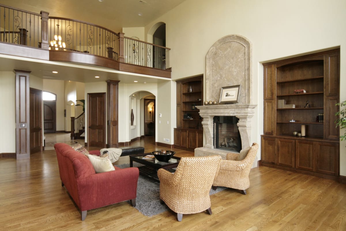 A family room with a stone fireplace, built-in shelves and a balcony above