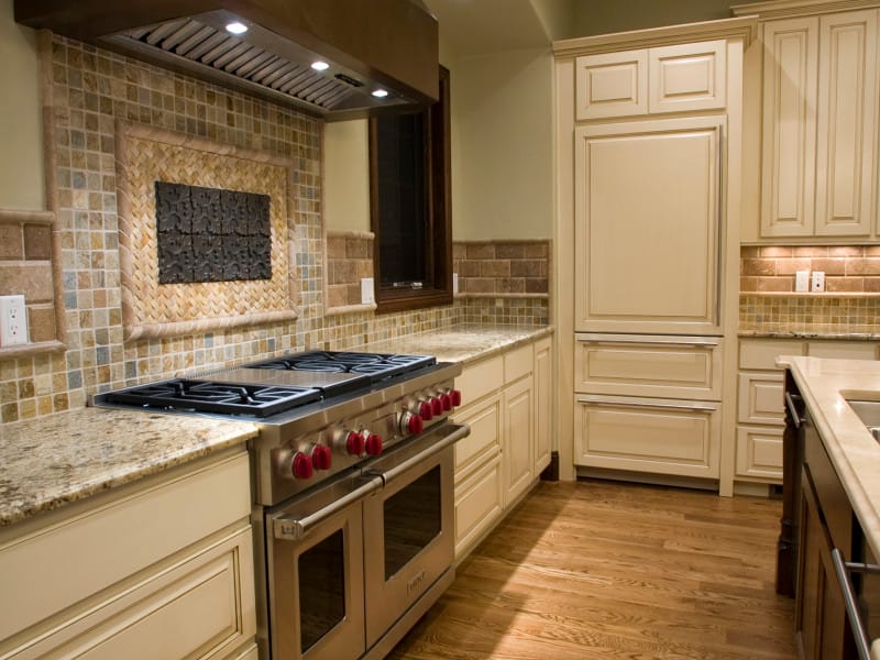 A kitchen with a professional range, tiled backsplash and cream cabinetry