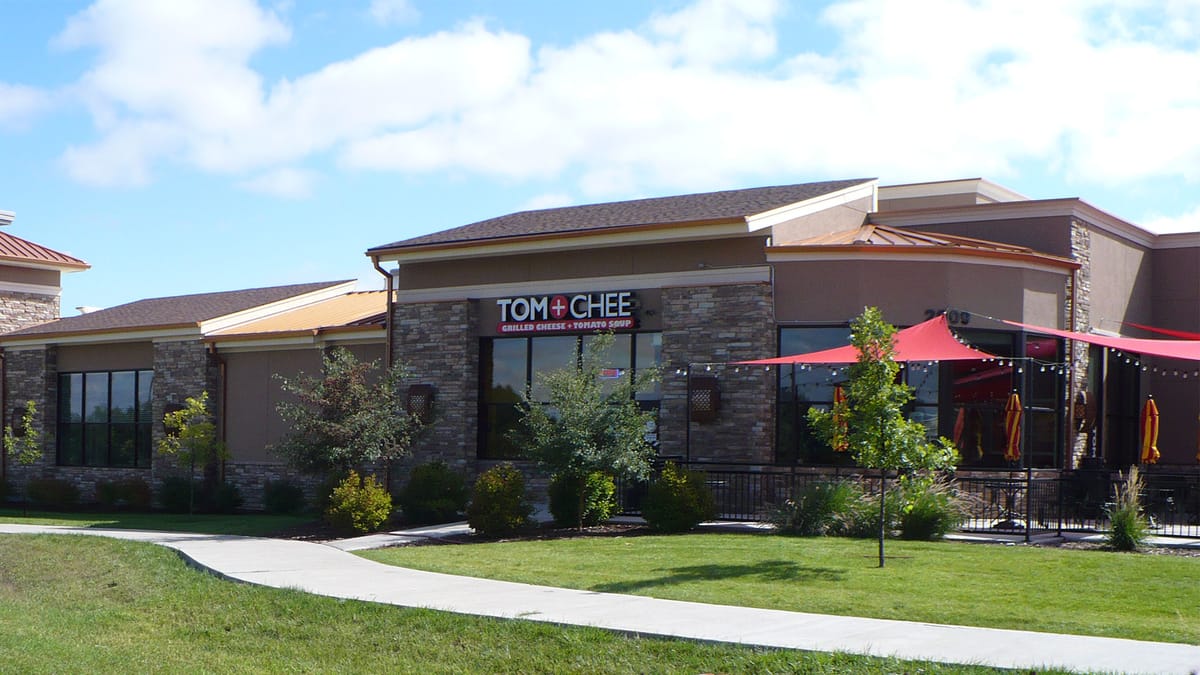 A stone and stucco retail building with a red awning over the patio