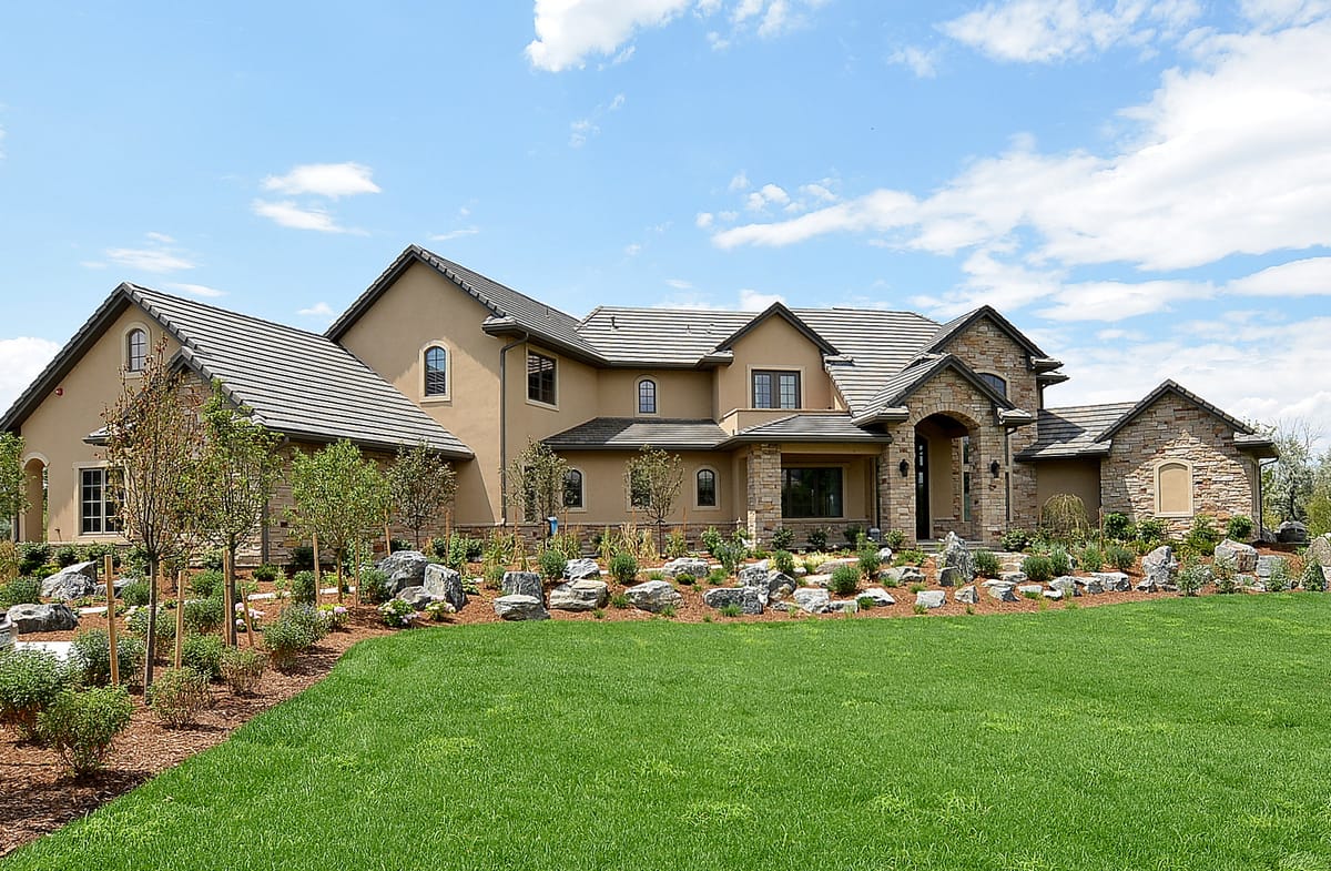 A long stone and stucco home behind a wide lawn and boulder plantings