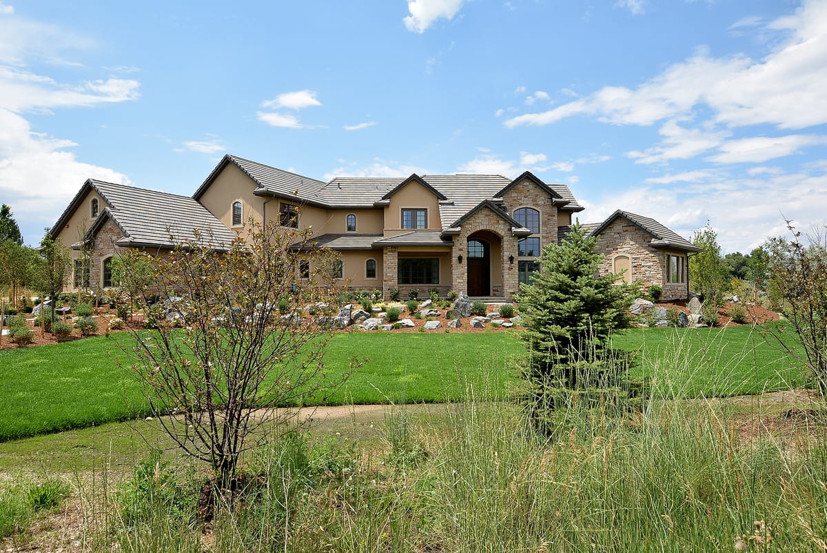 The same home seen across a meadow, with an evergreen in the foreground