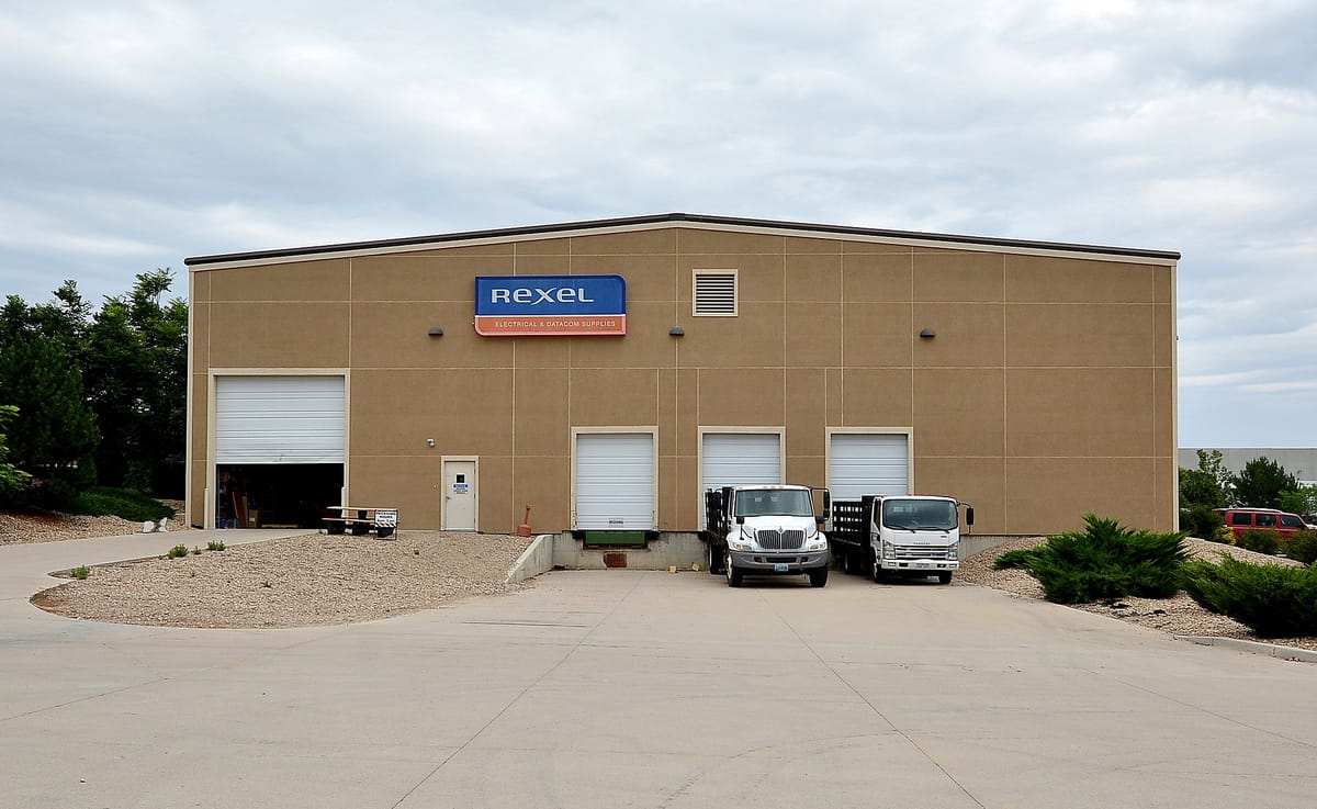 A tan warehouse with an overhead door and vans parked outside