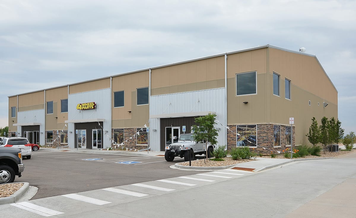 A tan metal warehouse with a stone-faced retail entry and parking bays