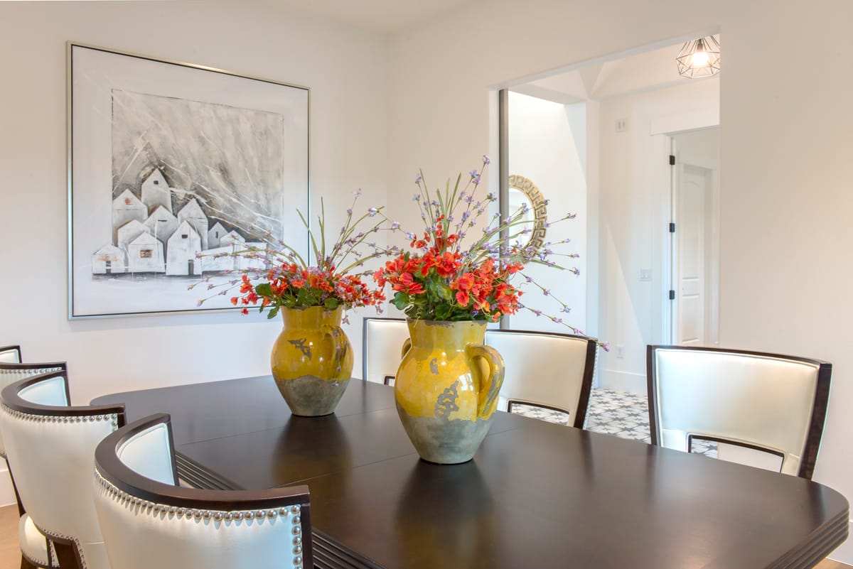 A formal dining room with a dark wood table, white chairs and a framed sketch