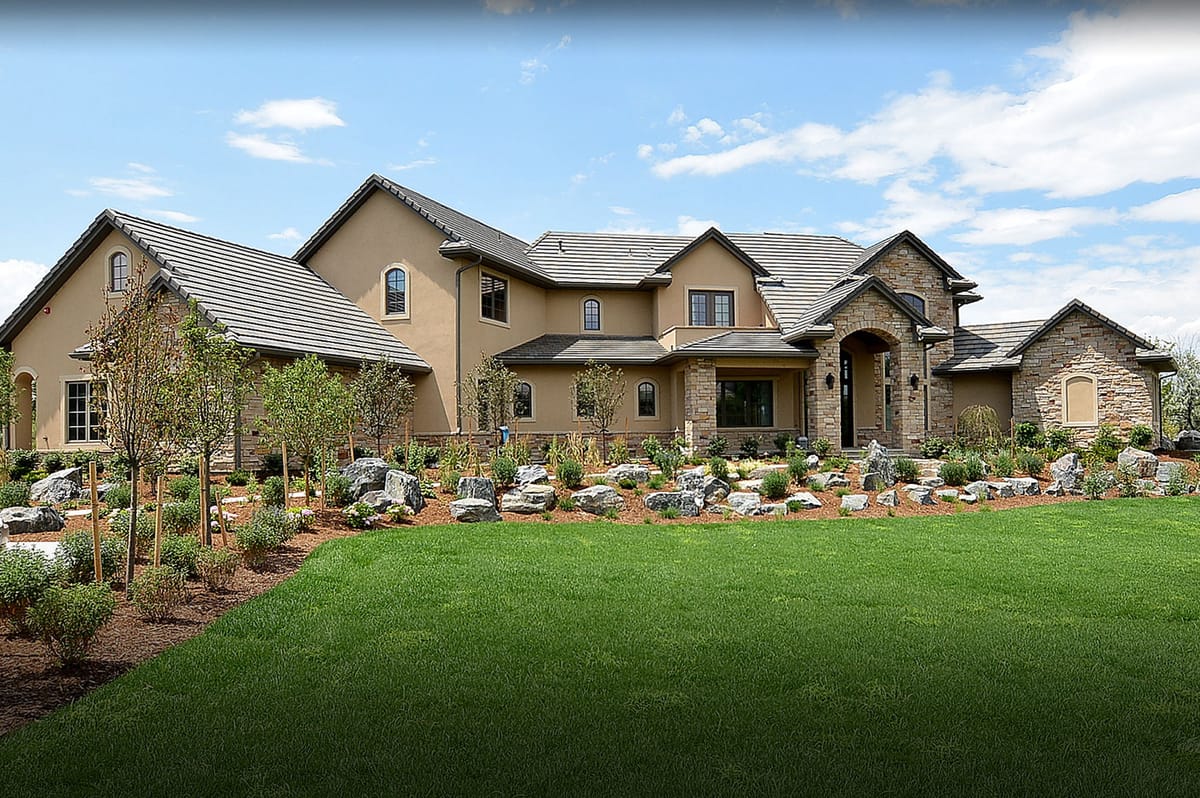 A stone and stucco custom home with a tile roof, set behind a landscaped lawn