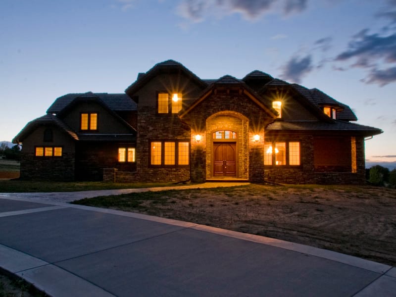 A stone custom home lit from within at dusk