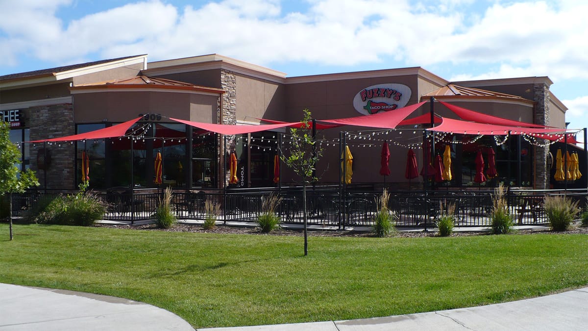 A restaurant with red patio umbrellas and a stone and stucco exterior