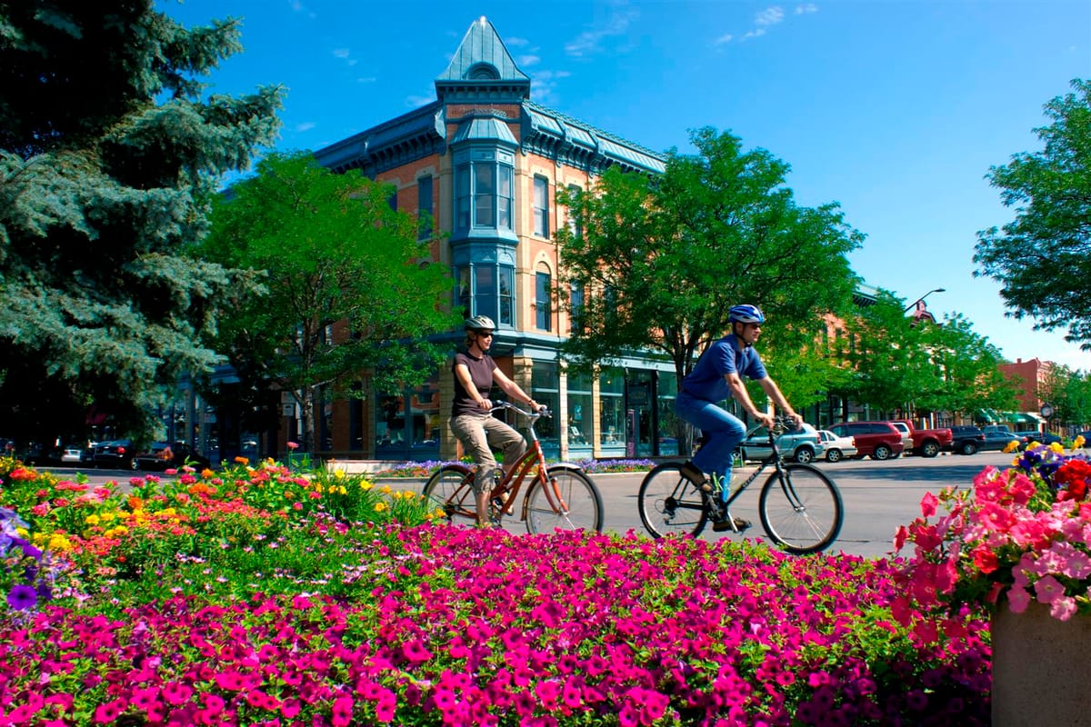 Cyclists riding past flower beds on Old Town Square in Fort Collins