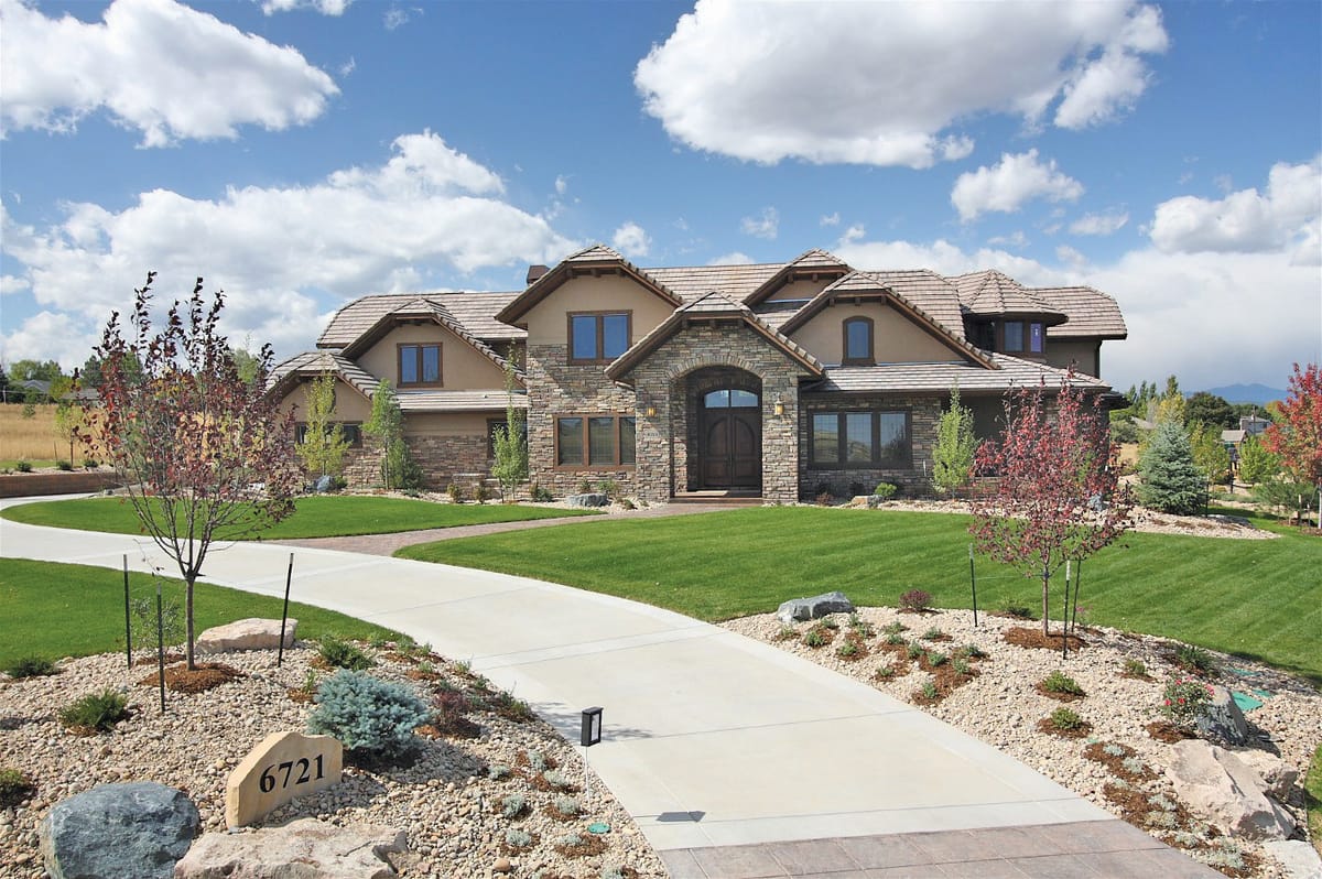 A stone and timber Niwot Hills home behind a curving driveway and young trees