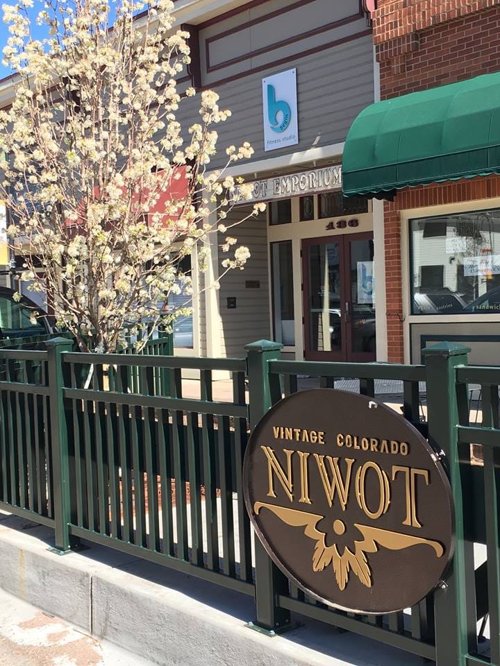 A carved wooden Niwot sign in front of historic downtown storefronts